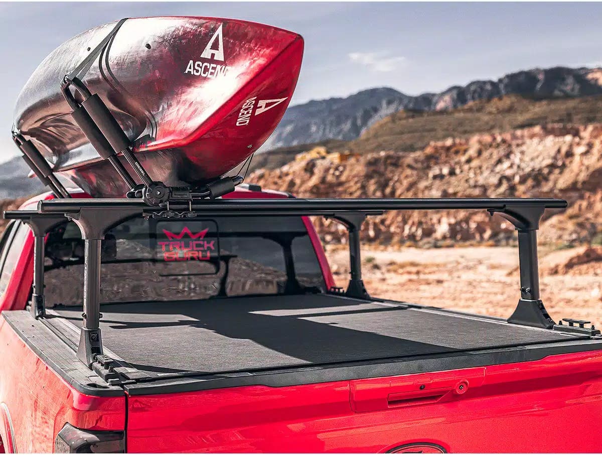 BAK Revolver X4TS bed cover on back of a red truck with a ladder rack installed and a kayak loaded